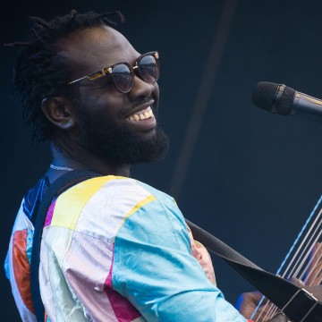 Man in sunglasses and multicolour top in front of mic smiling