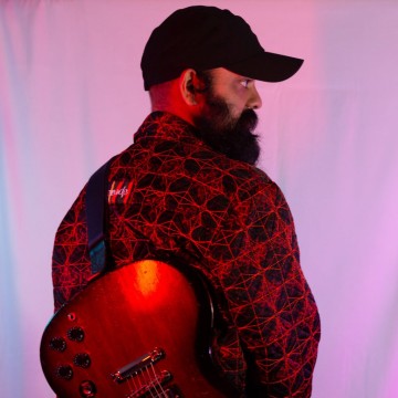 Man back turned, guitar on back and wearing cap on pink background with