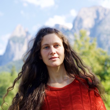 Woman long brown hair in red jumper against green trees, mountains and blue sky
