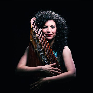 Woman curly hair on black background embracing a qanun instrument