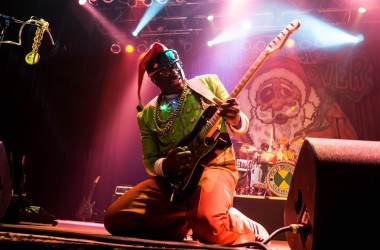 man in santa hat shredding guitar on pink lit stage
