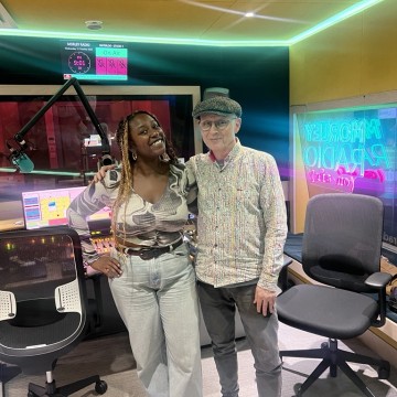 2 people standing smiling in Morley Radio studio, chairs either side