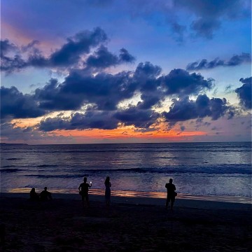 Blue tinted sky above ocean and people by water as sun sets