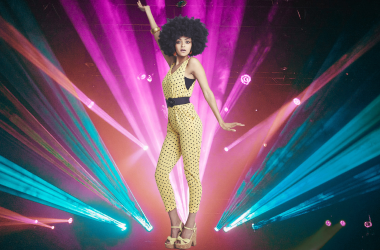 Woman with afro posing with one arm up in front of disco lights