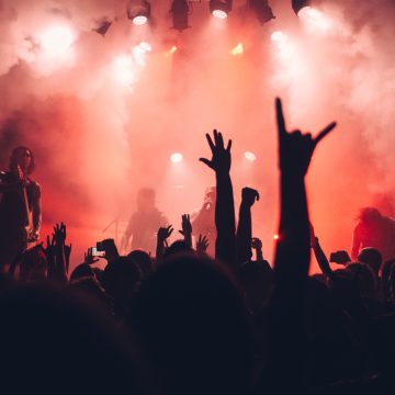 silhouette of hands in air at gig against red hazy stage and lights